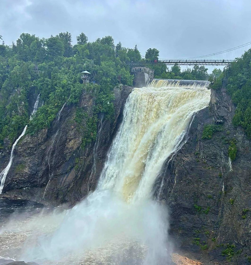 An image taken from a bridge above Montmorency Falls, facing the falls as the water flows over a rocky cliff face